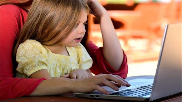 Young girl sitting on her mother's knee, while both looking at a laptop